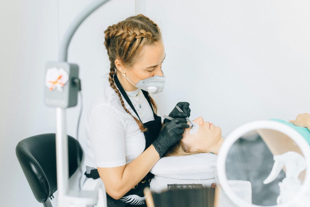 Beautician wearing gloves applies a face treatment to woman lying down in spa setting.